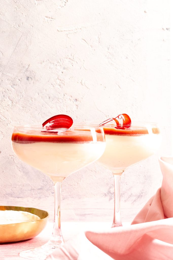 Two champagne coupes filled with vanilla panna cotta and rhubarb coulis.