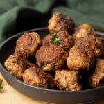 A black plate with lamb meatballs in a wooden board.