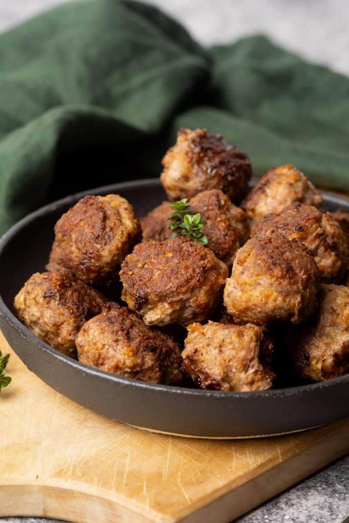 A black plate with lamb meatballs in a wooden board.