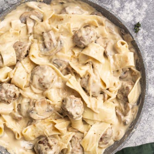 Meatballs in a creamy sauce added to pappardelle in a large pan.