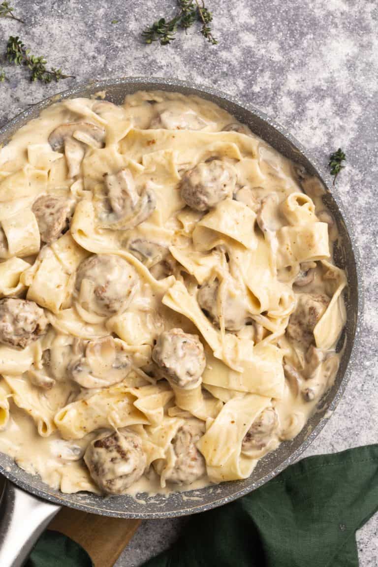 Meatballs in a creamy sauce added to pappardelle in a large pan.