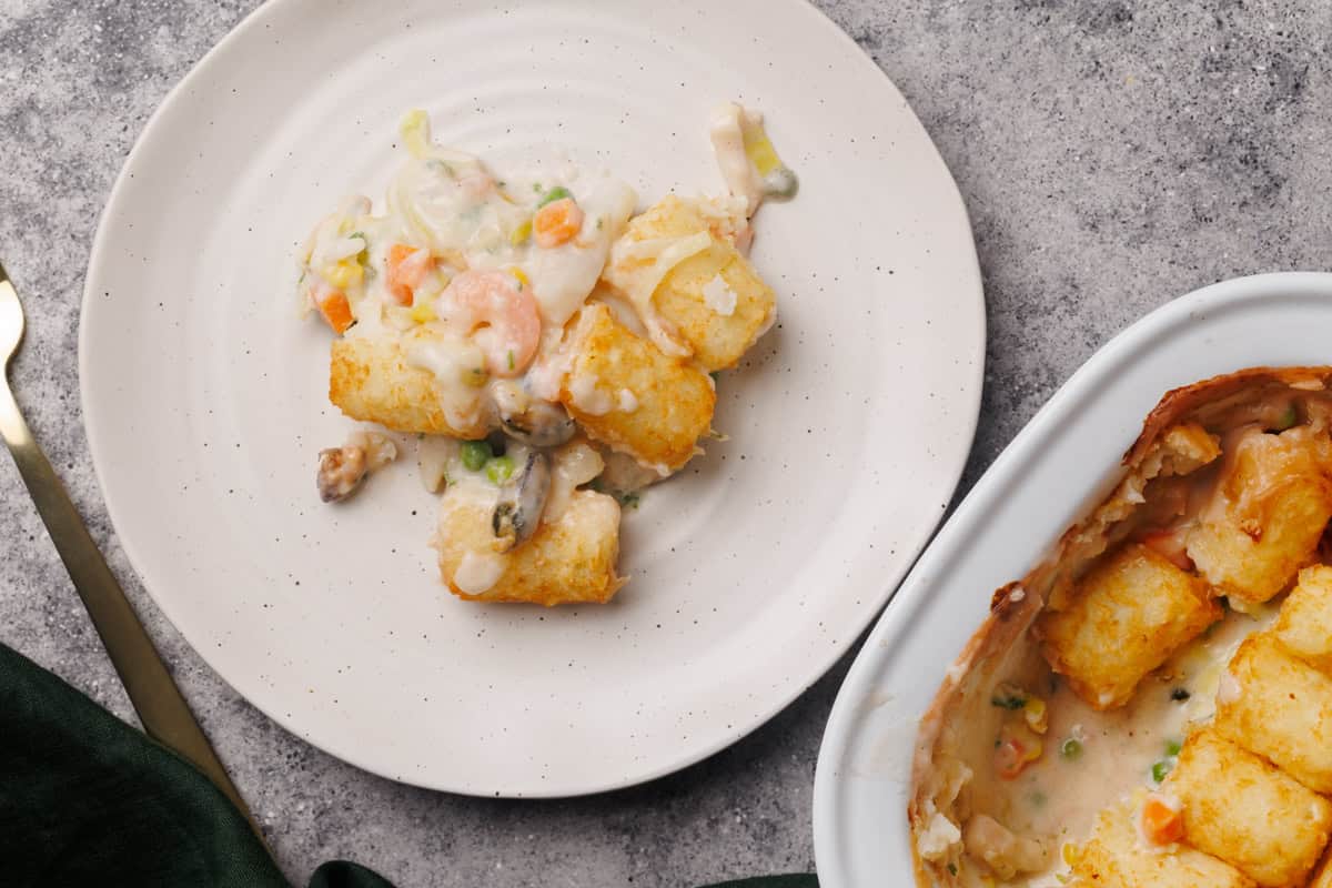 A serving of seafood pie on a white plate next to the casserole dish.