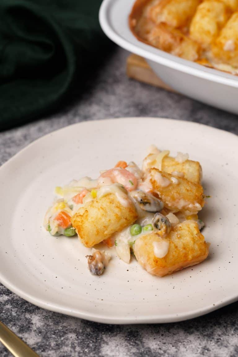 A serving of seafood pie on a white plate next to the casserole dish.