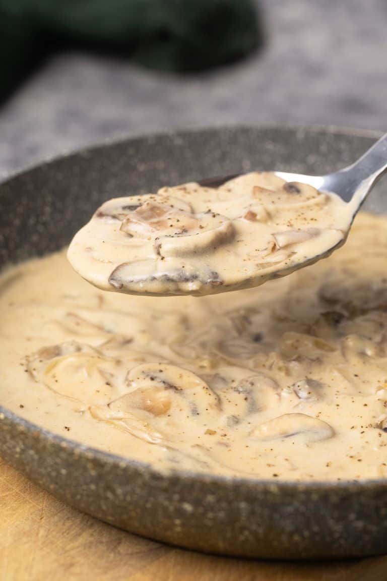 Mushroom sour cream sauce in a grey pan being scooped out.