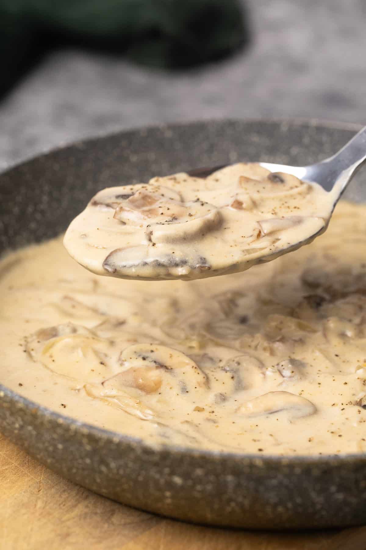 Mushroom sour cream sauce in a grey pan being scooped out.
