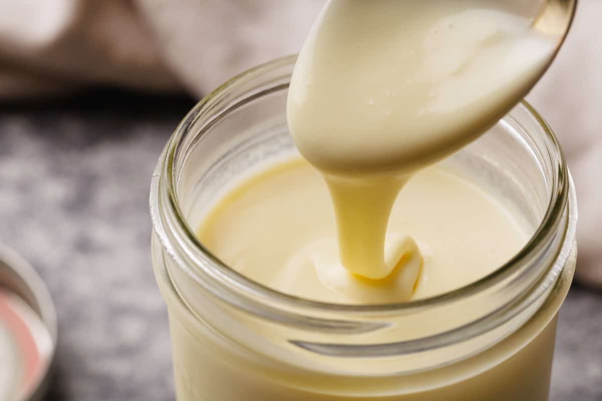 Condensed milk being scooped out of a jar with a large spoon.