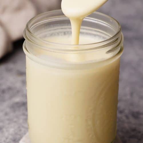 Condensed milk being scooped out of a jar with a large spoon.