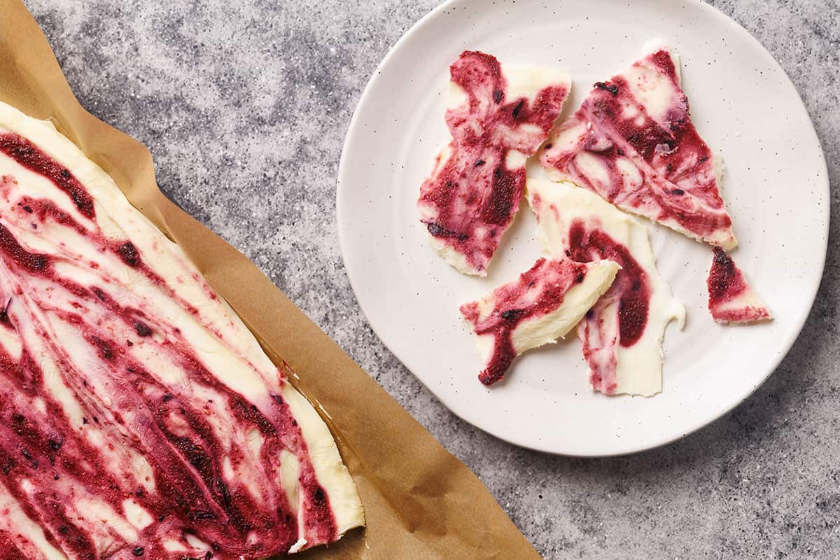 Frozen yogurt bark with berries on a baking sheet and broken into pieces on a side plate.