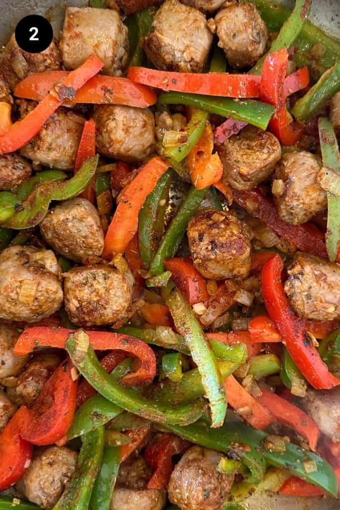 Beef sausage pieces, onion, bell peppers, and spices being cooked in a large pan.