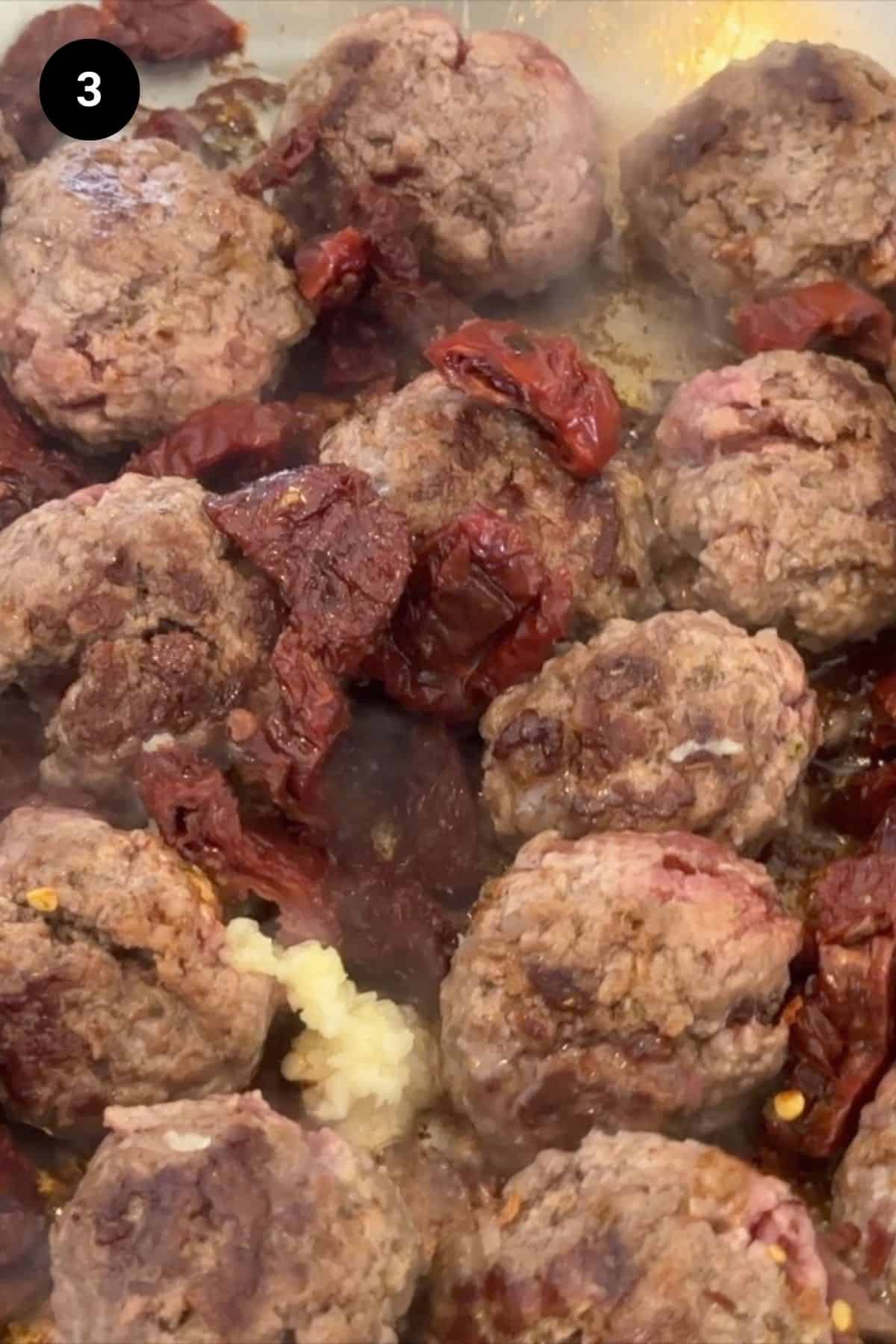 Cooked meatballs, broth, and sun dried tomatoes in a pan.