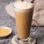 Latte in a tall glass cup on a marble coaster next to toasted milk and a napkin.