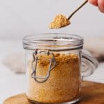 Milk powder being scooped out of a glass container.