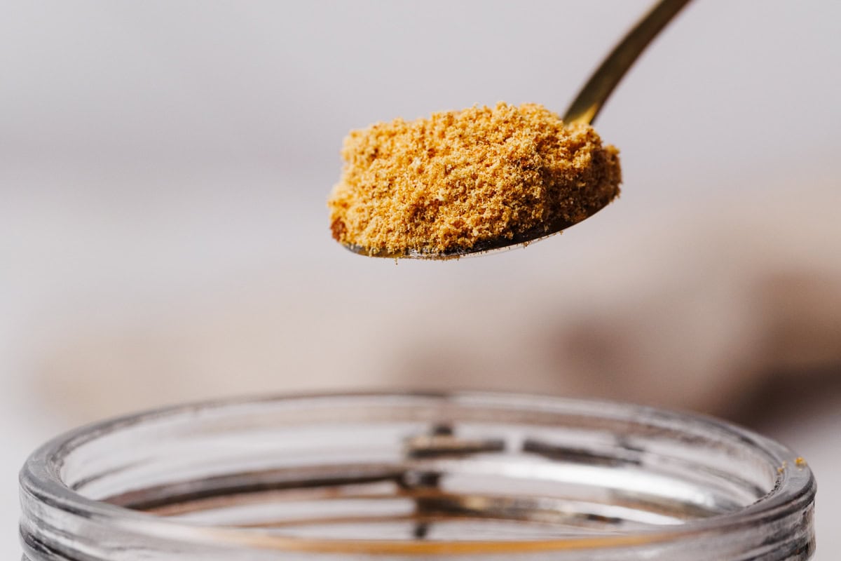 Toasted milk powder being scooped out of a glass container.