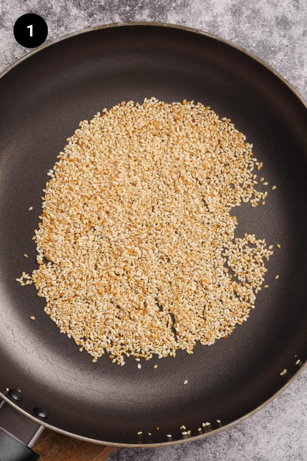 Sesame seeds being toasted in a black pan.