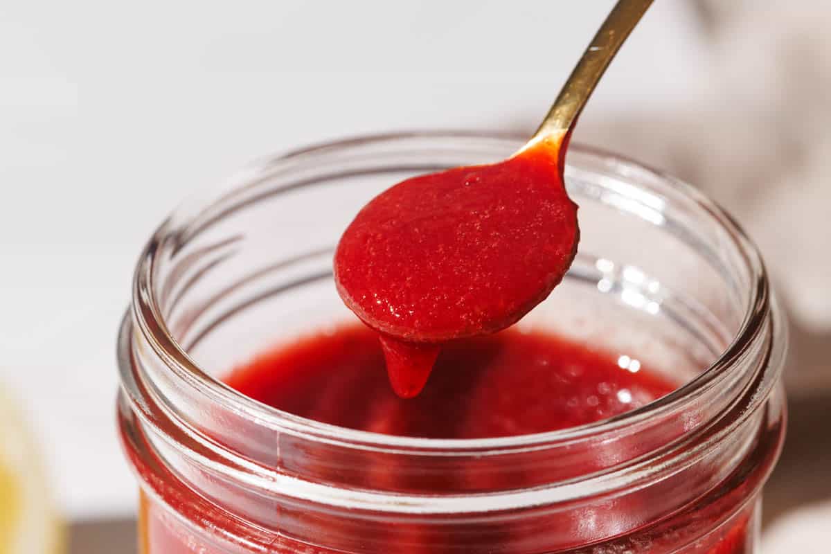 Strawberry puree being scooped out of a mason jar.