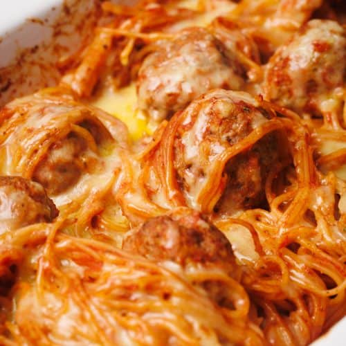 Spaghetti and meatballs baked in a white casserole dish, covered with melted cheese.