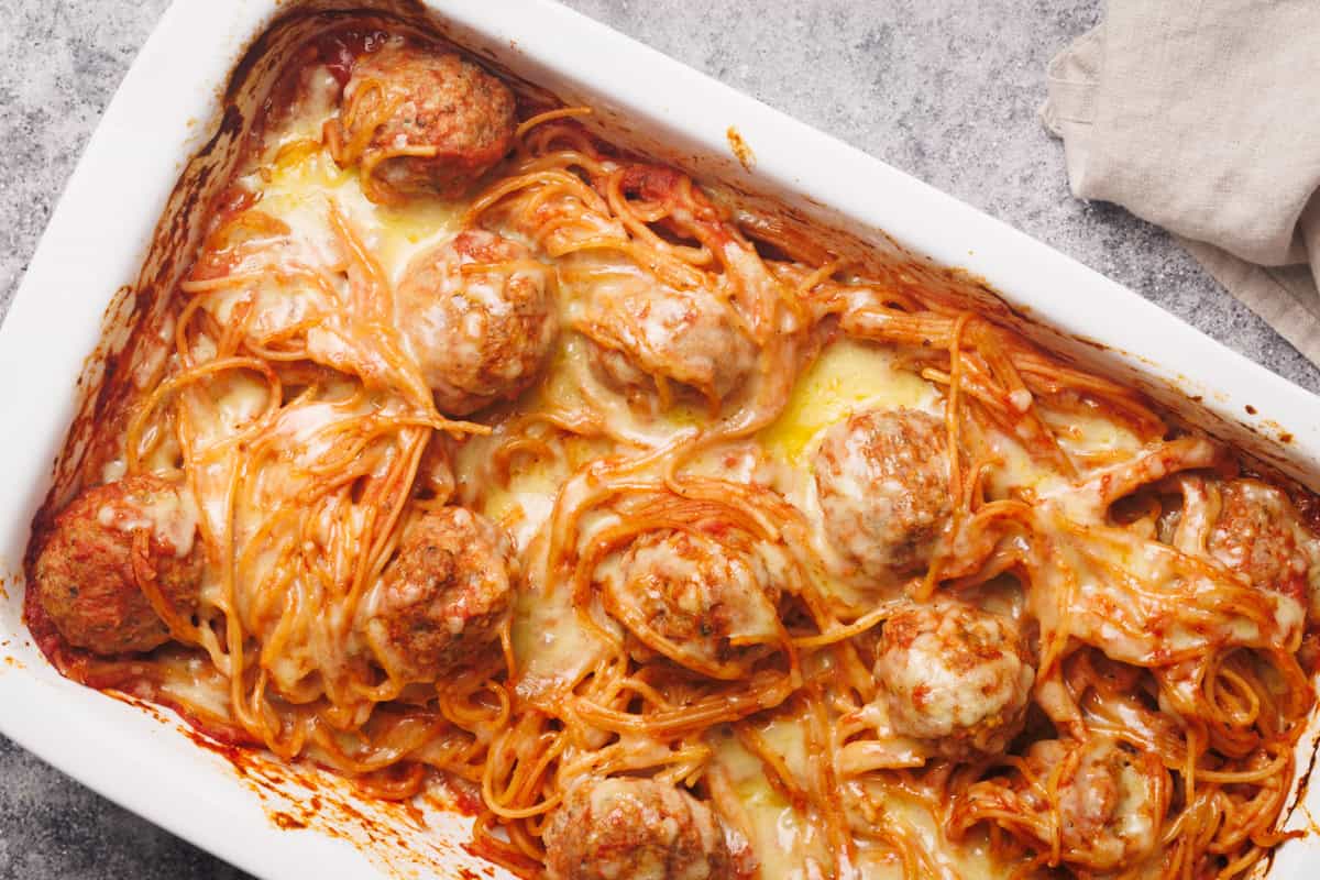 Spaghetti and meatballs baked in a white casserole dish, covered with melted cheese.