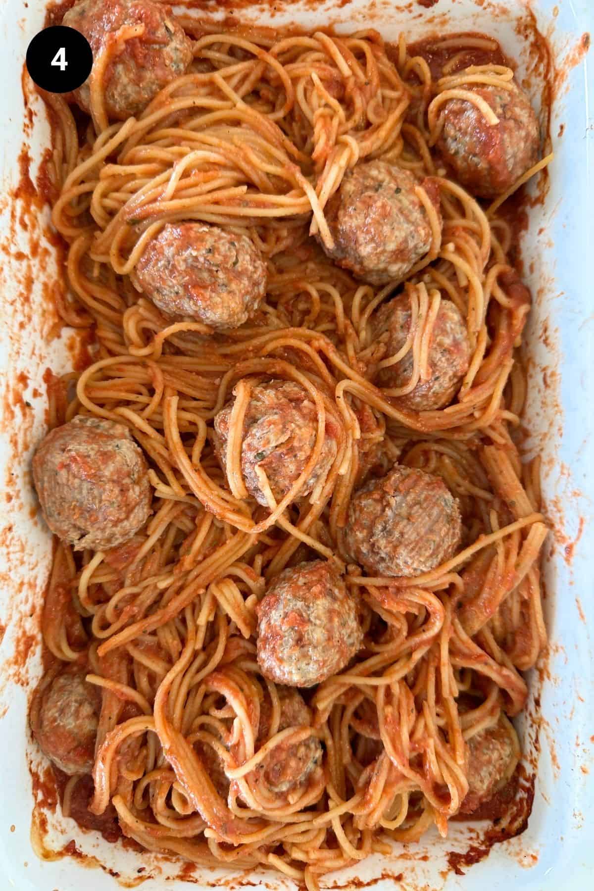 Spaghetti and meatballs in a white casserole dish before being baked.