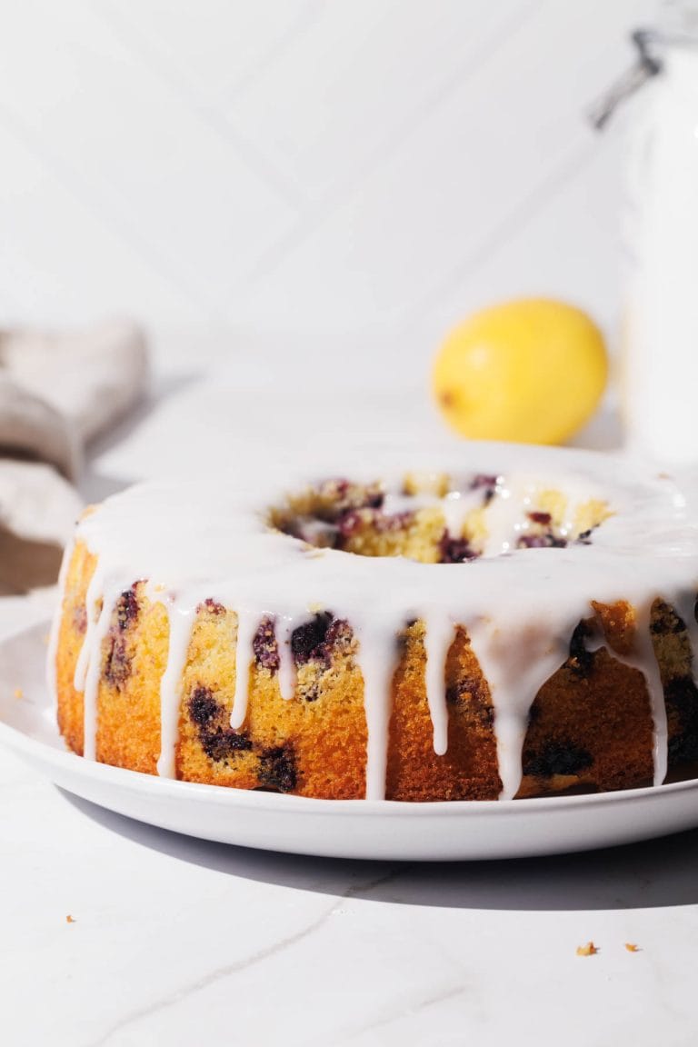 A pound cake in ring form on a white plate with white icing.