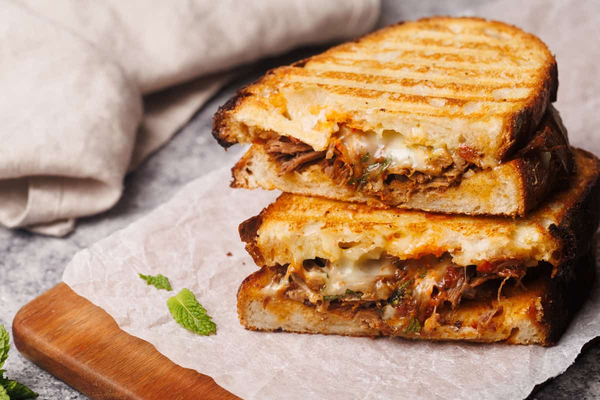 Grilled lamb sandwich cut in half on a wooden board.