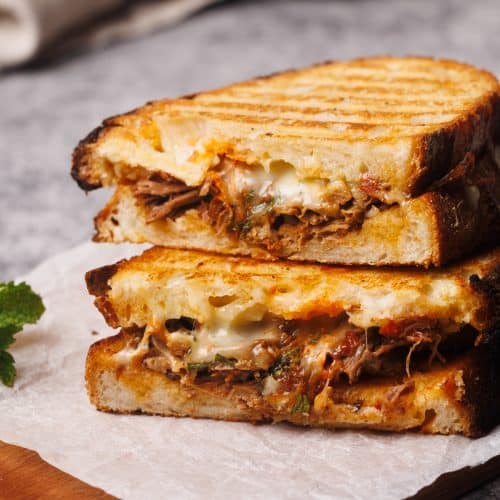 Grilled lamb sandwich cut in half on a wooden board.