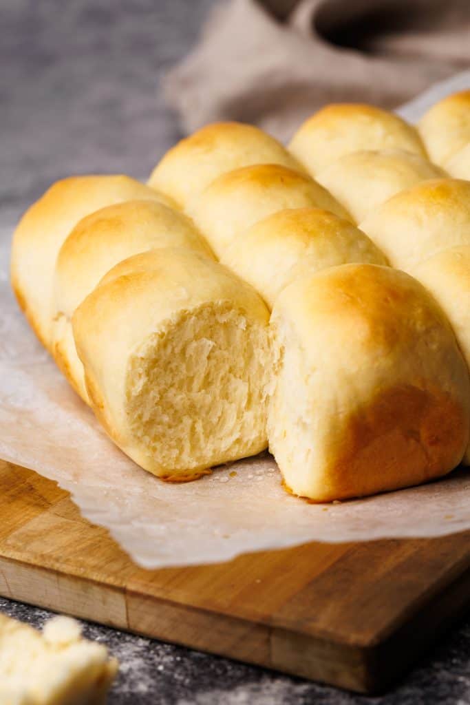 Dinner rolls on a parchment paper lined wooden board.