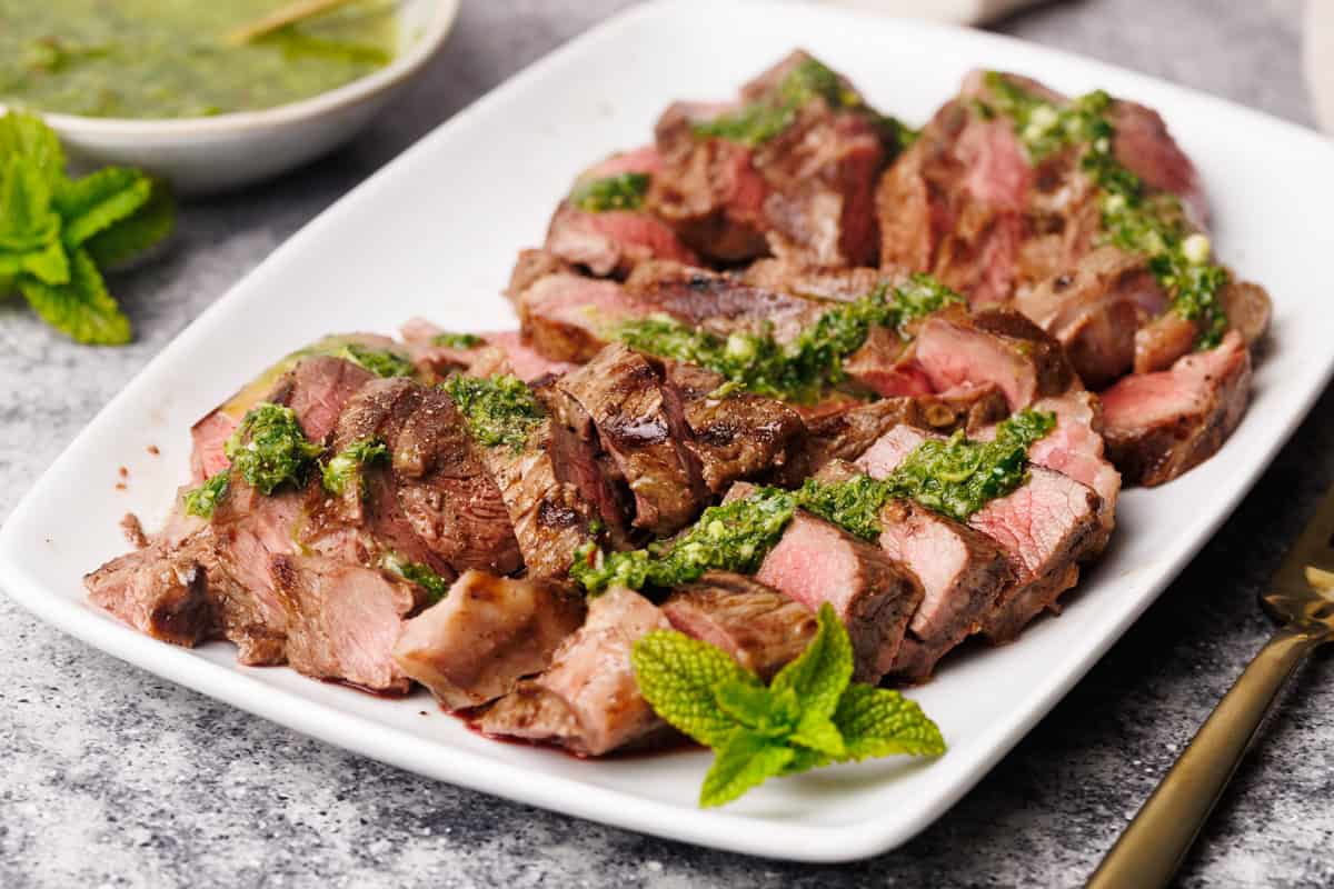 Steak pieces on a white serving plate with a mint sauce drizzled over.