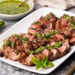 Steak pieces on a white serving plate with a mint sauce drizzled over.