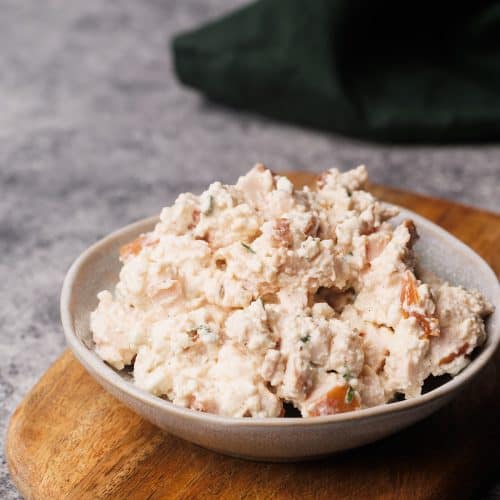 Smoked chicken salad in a small bowl on a wooden board.