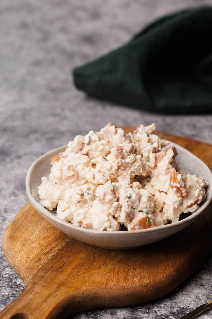 Smoked chicken salad in a small bowl on a wooden board.
