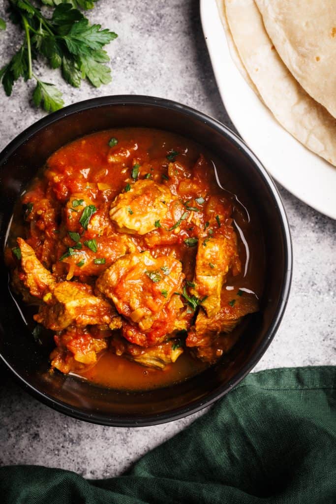 A black bowl filled with lamb curry next to naan bread and a green napkin.