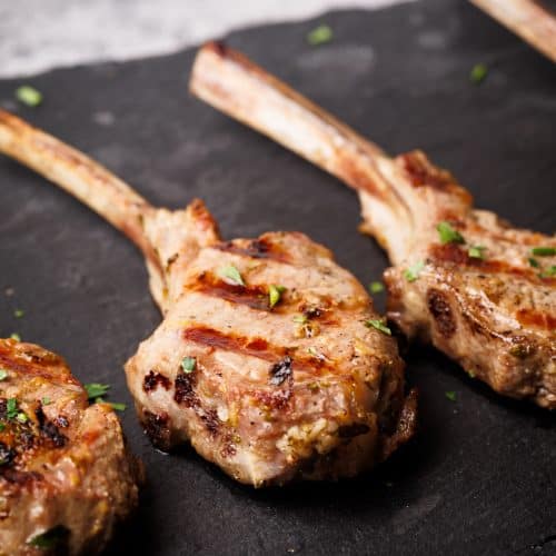 Grilled lamb lollipops on a black slate.