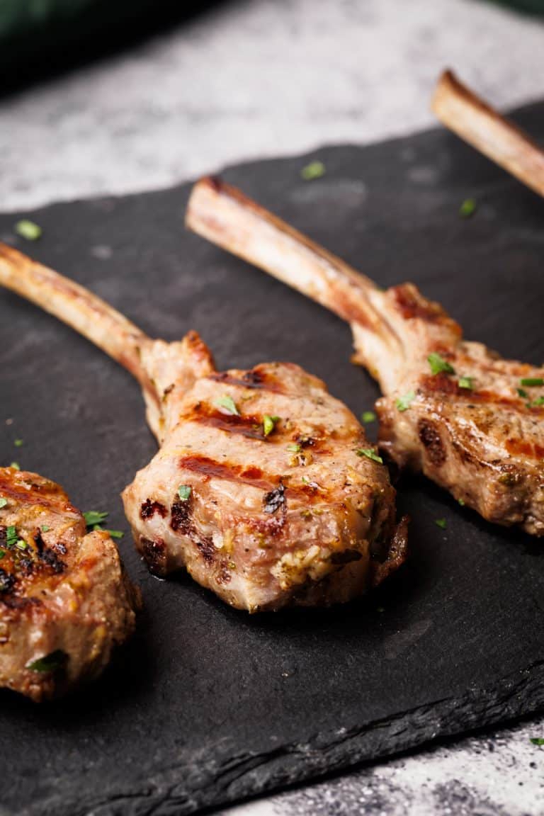 Grilled lamb lollipops on a black slate.