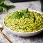 Mint pesto in a small white bowl next to a green napkin and golden spoon.