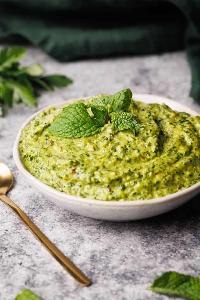 Mint pesto in a small white bowl next to a green napkin and golden spoon.