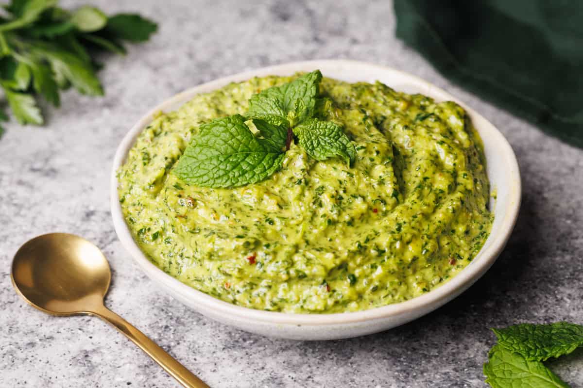 Mint pesto in a small white bowl next to a green napkin and golden spoon.