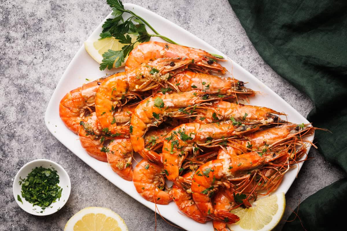 Cooked tiger shrimp on a white plate next to a lemon and parsley.