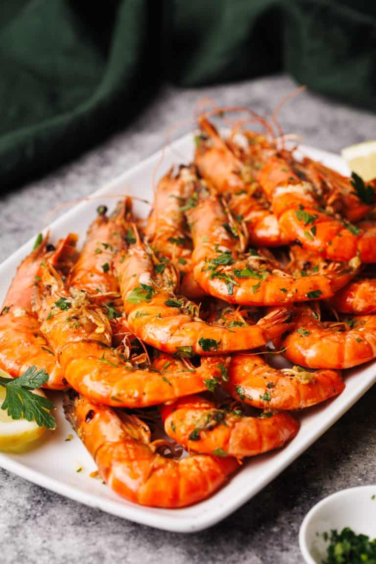 Cooked tiger shrimp on a white plate next to a lemon and parsley.