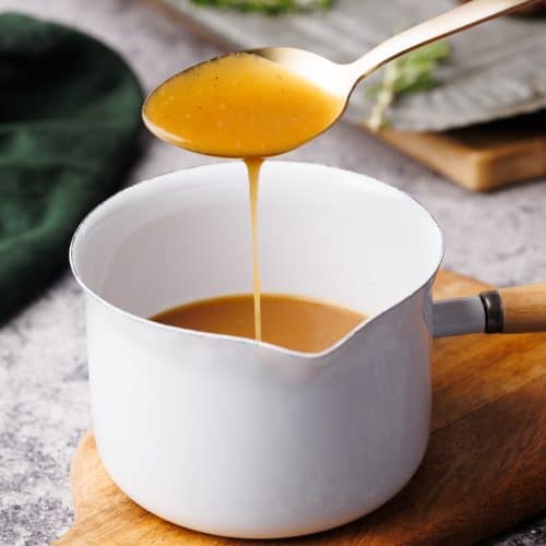 Lamb gravy in a small white saucepan on a wooden board.