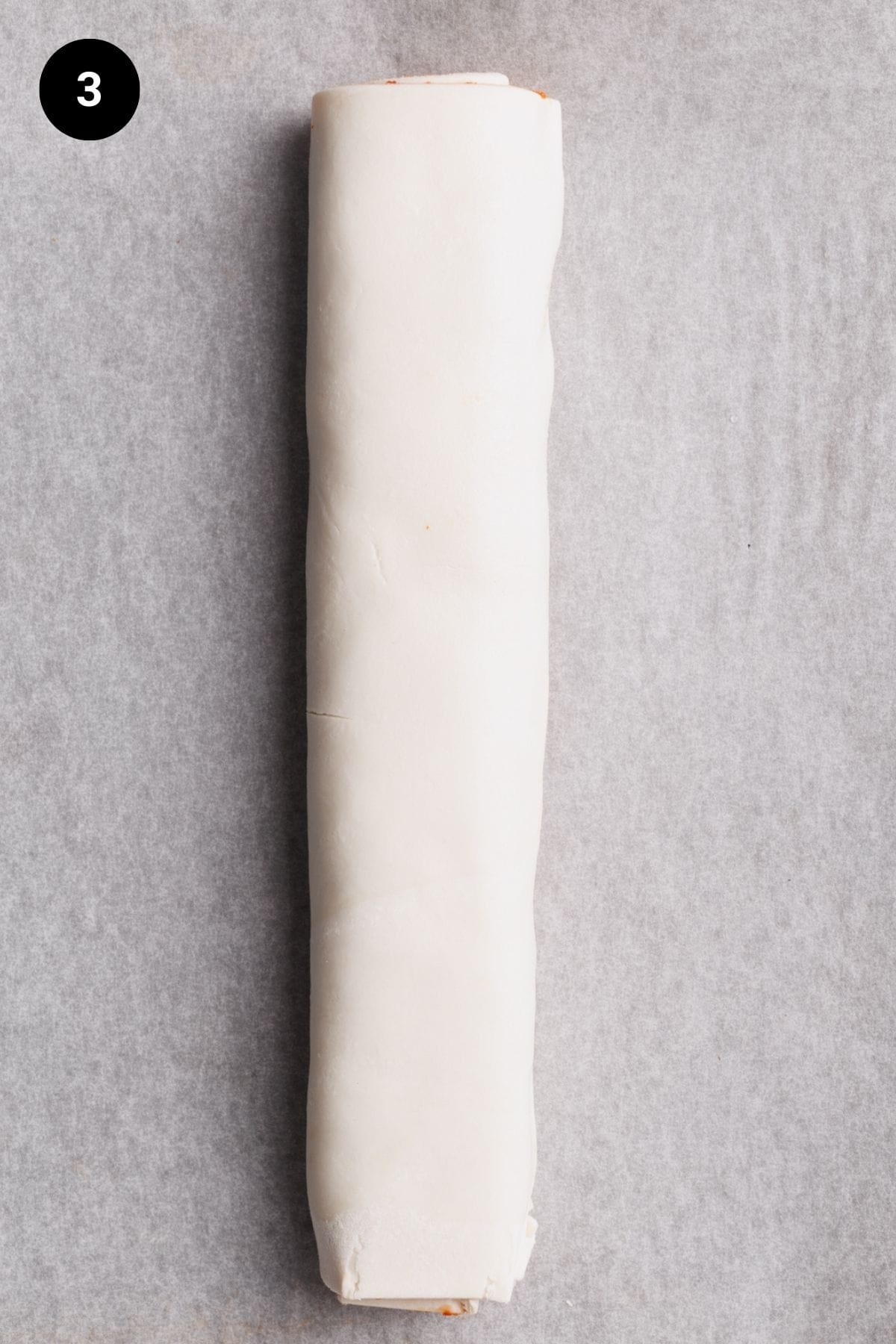 Filled puff pastry roll on a baking sheet.