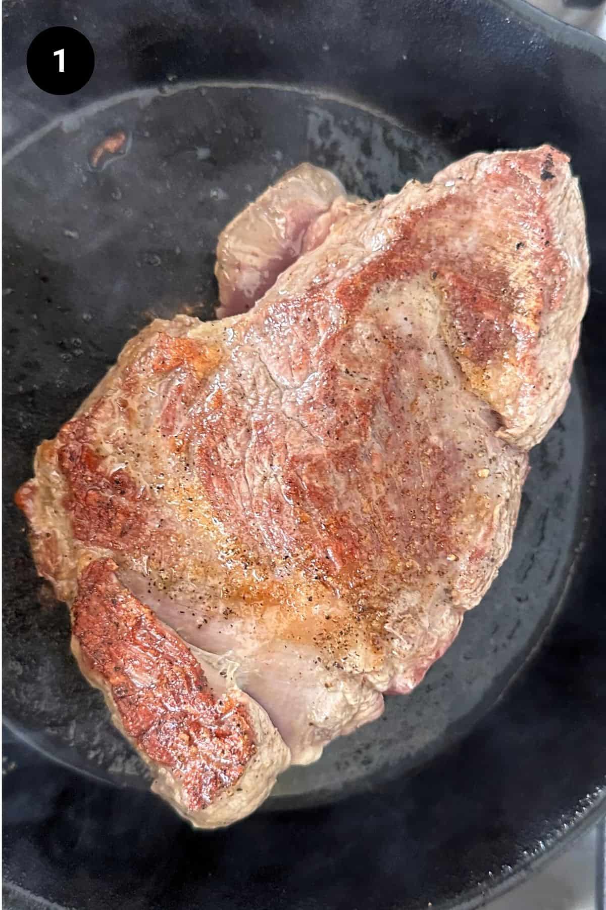 Lamb roast being seared in a cast iron pan.