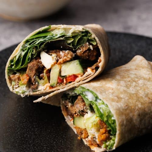 A lamb wrap cut in half on a black plate.