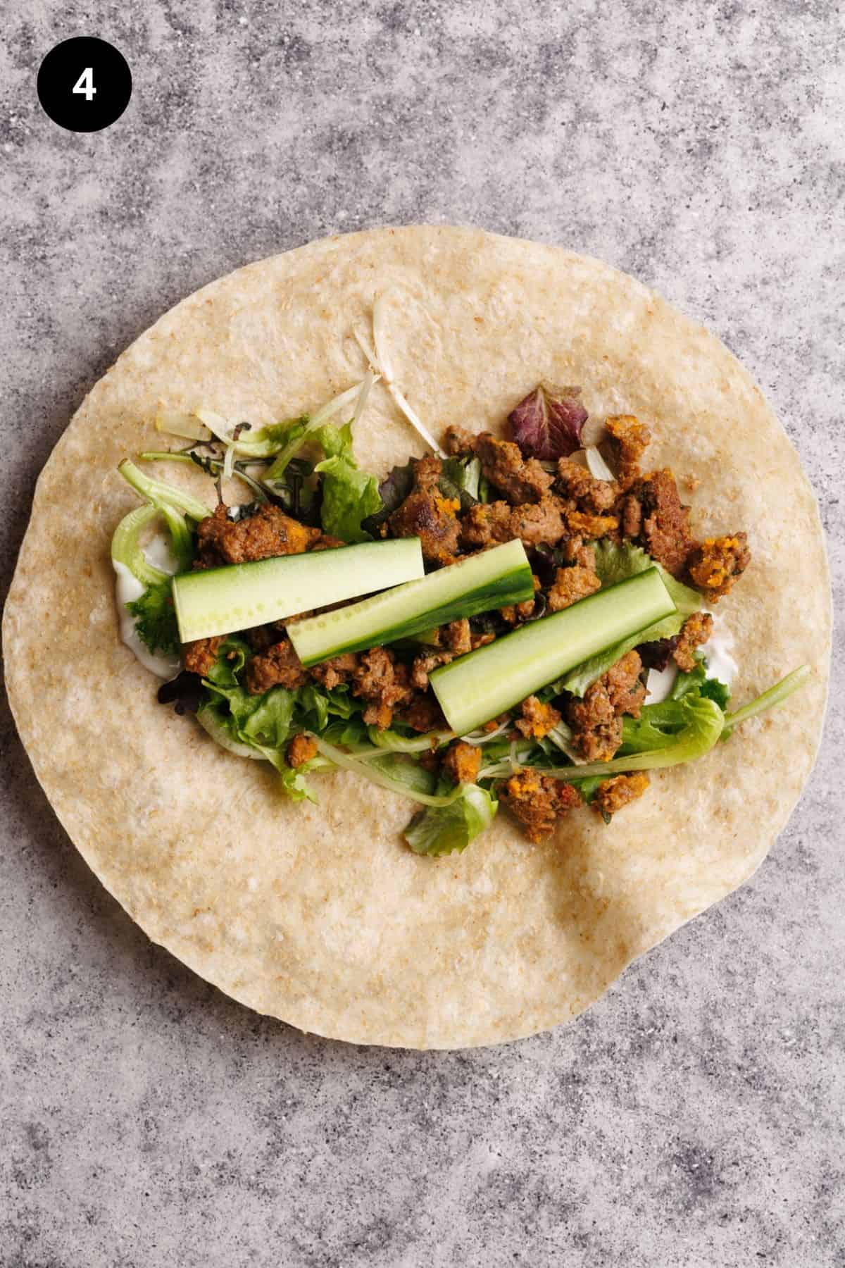Salad, cucumber, and cooked sausage on a flour tortilla.
