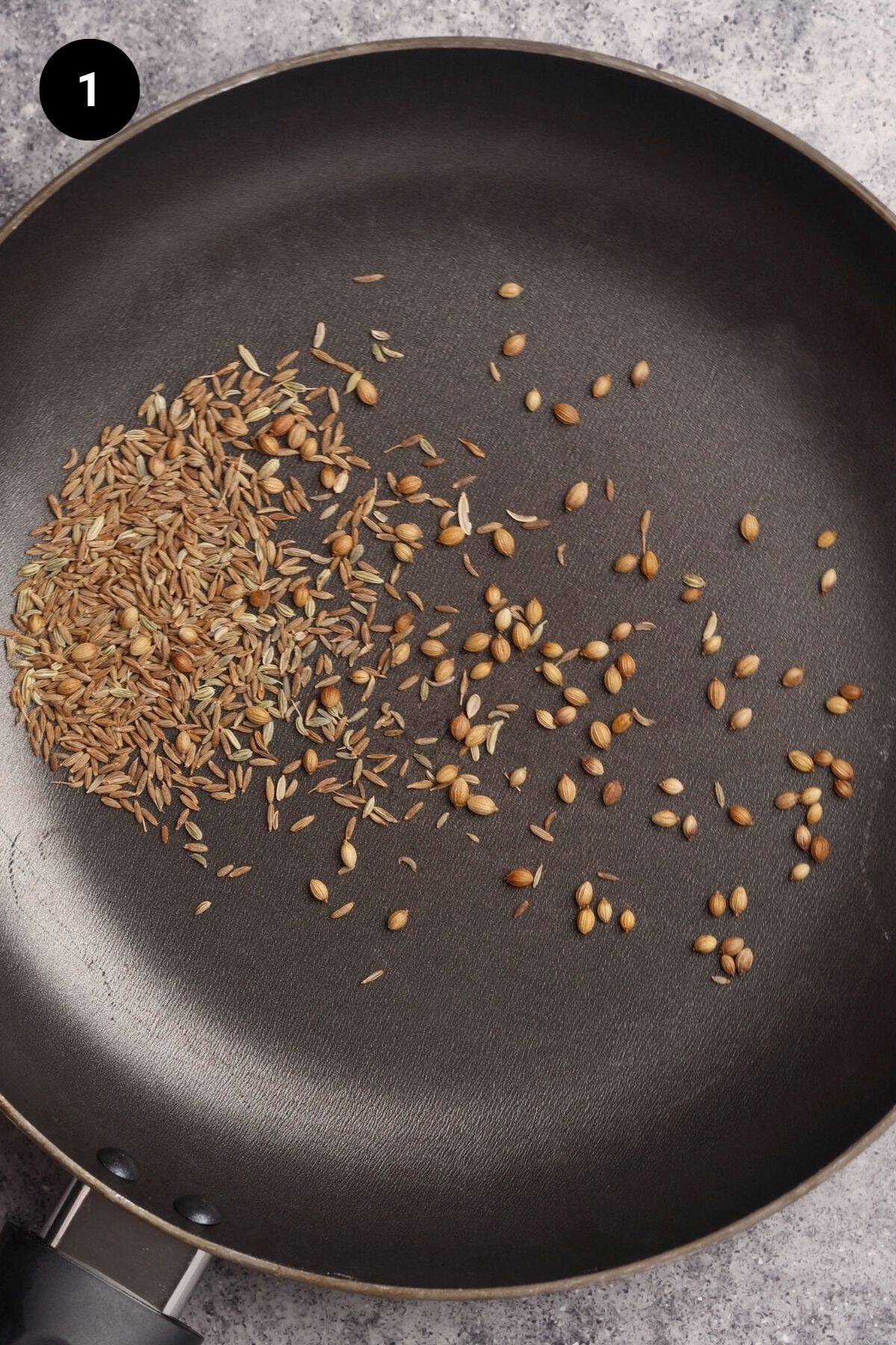 Spices being dry roasted in a black pan.