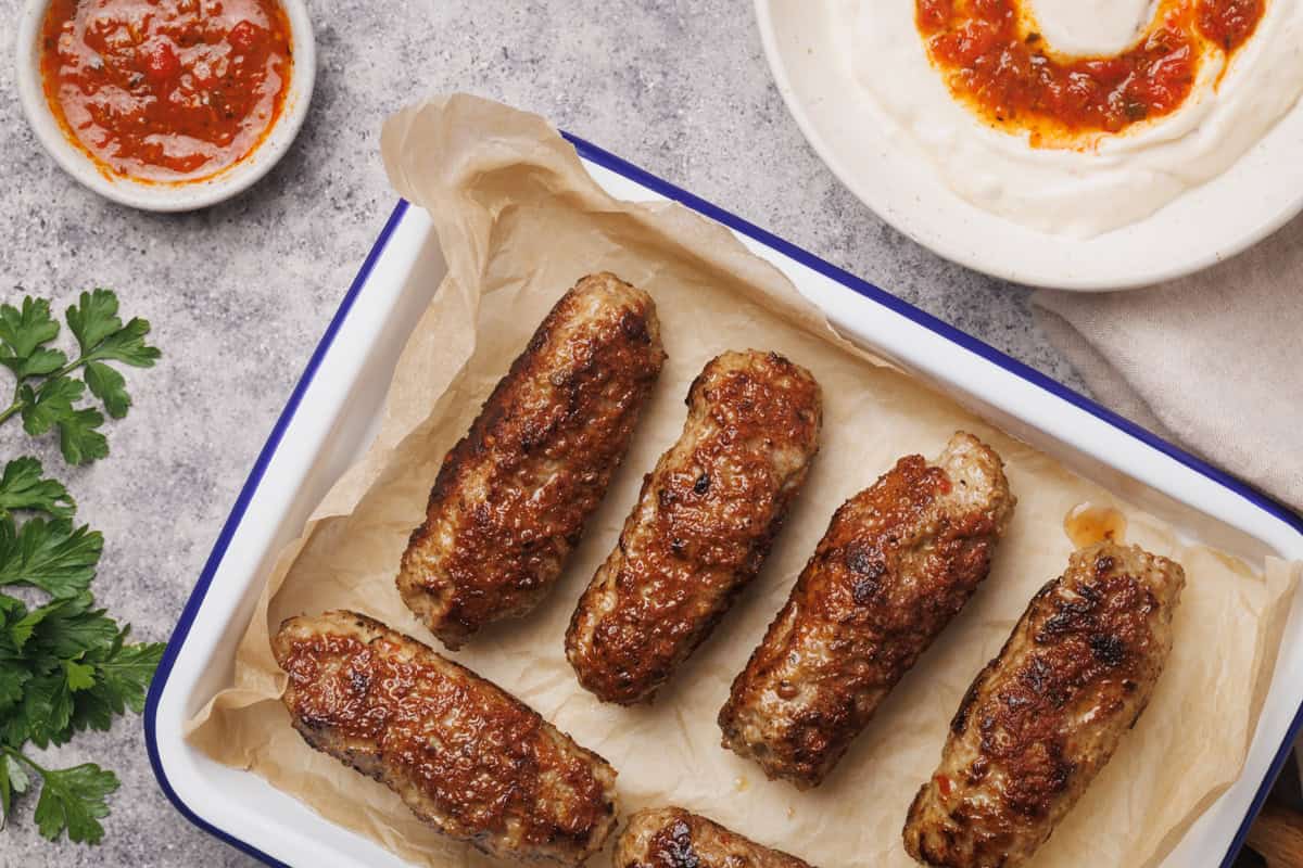 An enamel tray with lamb sausages next to dips.