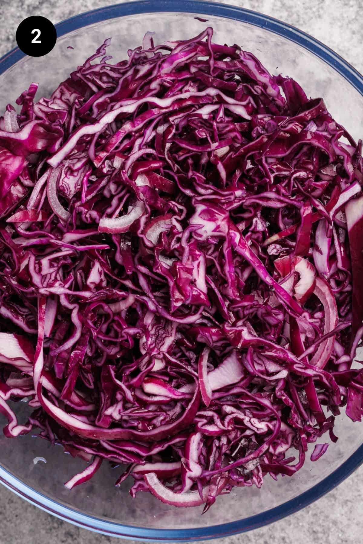 Red cabbage, salt, and caraway seeds mixed in a large glass bowl.