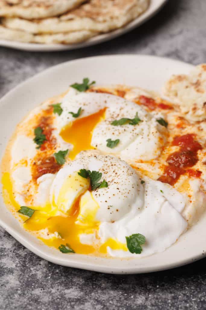 Turkish eggs with harissa on a white plate next to flatbread.