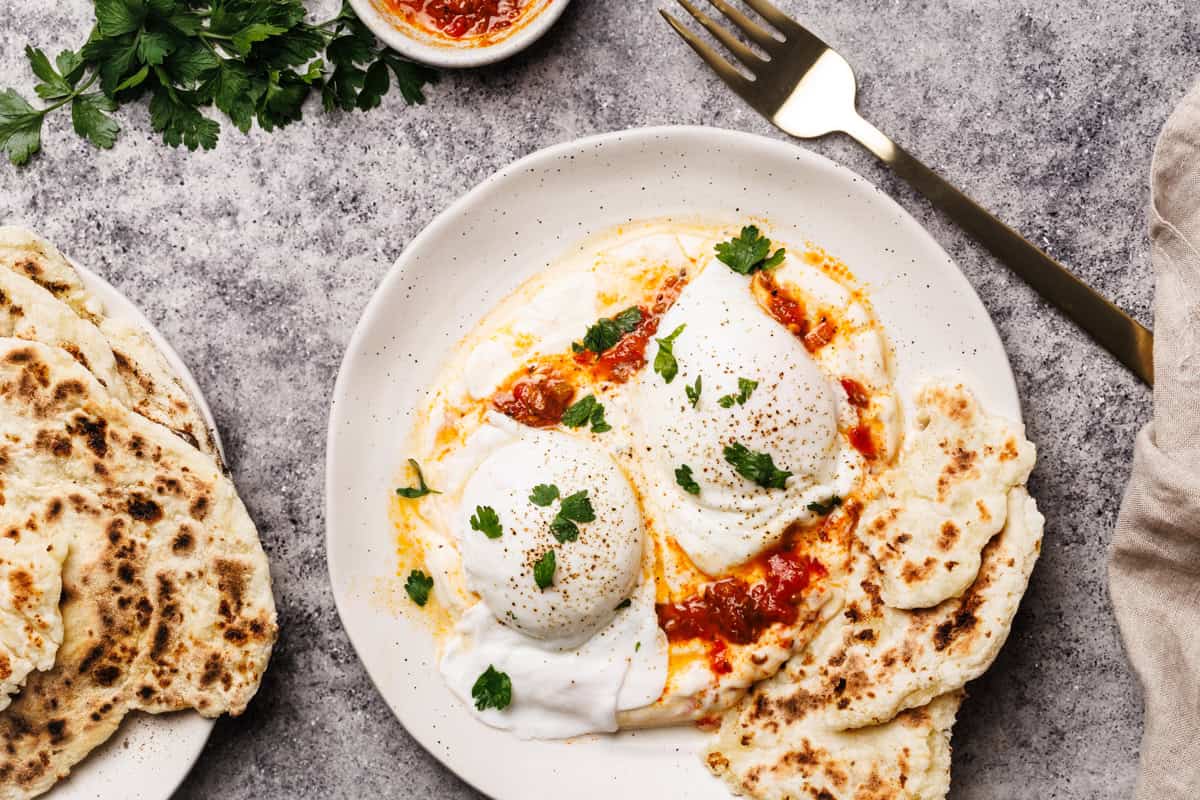 Turkish eggs with harissa on a white plate next to flatbread.