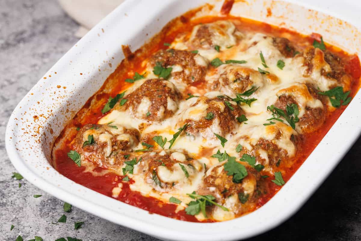 Baked harissa meatballs in a white casserole dish next to a linen tea towel.