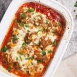 Baked meatballs in a white casserole dish next to a linen tea towel.
